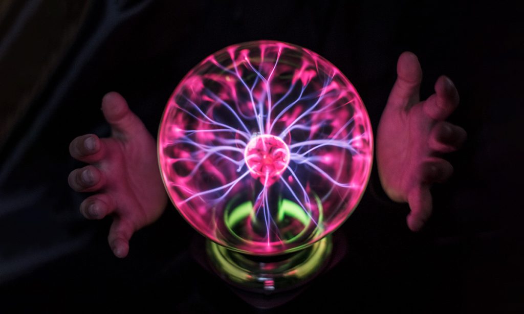 Hands surrounding a glowing pink plasma ball with electrical filaments against a dark background.